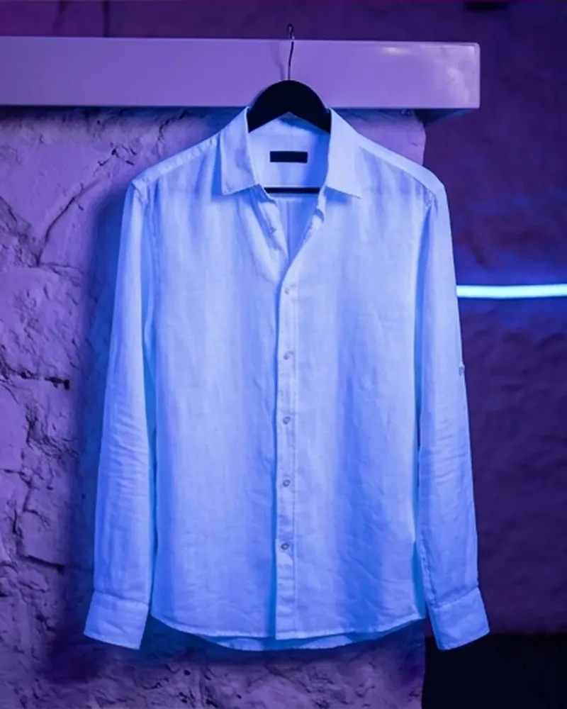 Camisa blanca colgada de una percha junto a la barra, bajo luz azul y violeta.
